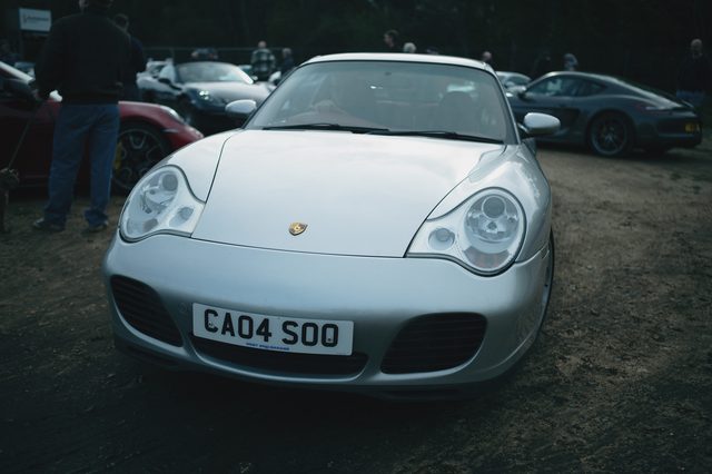 A silver Porsche 911 parked on the dirt car park, head-on.