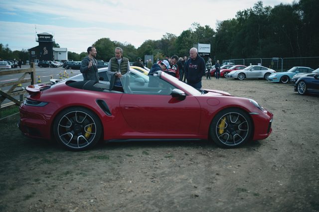 A red Porsche 911 convertible with yellow brake calipers, people behind.