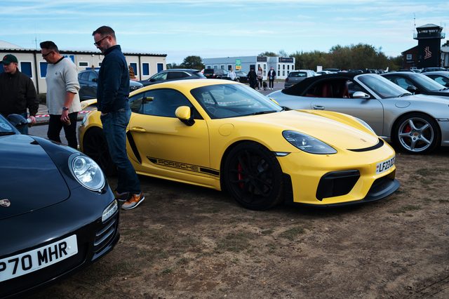A yellow Porsche with a black side stripe among parked cars, two men beside it.