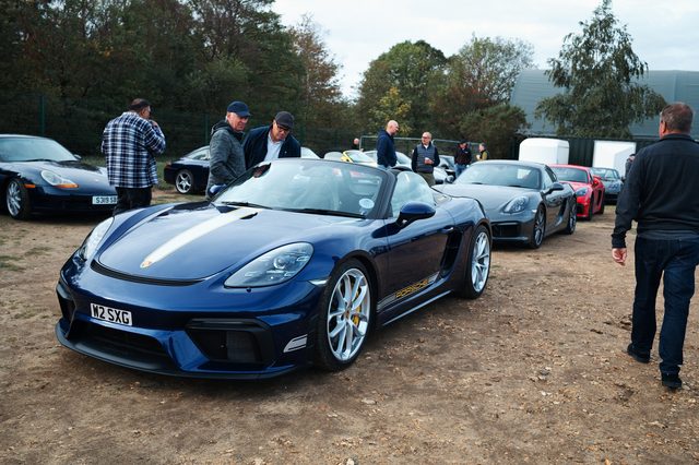 A dark blue Porsche convertible with silver stripes, owners chatting nearby.