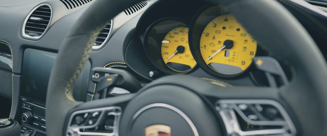The steering wheel and yellow dials of a Porsche cockpit.
