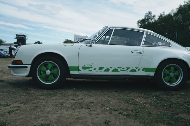 A white classic Porsche 911 with green Carrera script and green wheels, side on.