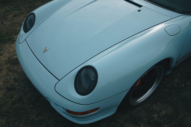 The headlamp and bonnet of a pale blue Porsche 911, close.