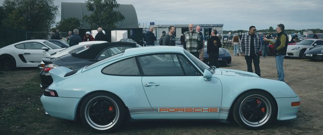 A pale blue classic Porsche 911 side on, people behind.