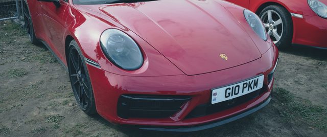 A red Porsche 911 head-on, another red Porsche behind.