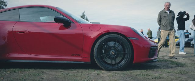 A red Porsche 911 side on, a man standing beside it.