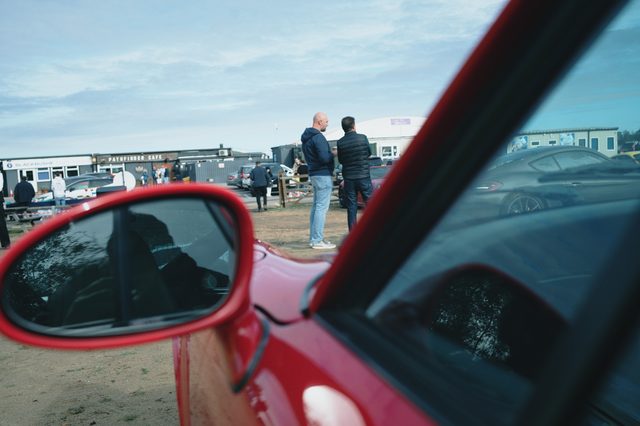 A red door mirror, the meet and the clubhouse beyond.