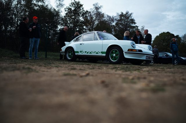 The white classic 911 seen low across the ground, the meet behind it.