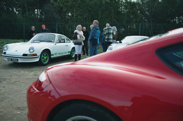 The white classic 911 framed past the curve of a red Porsche.