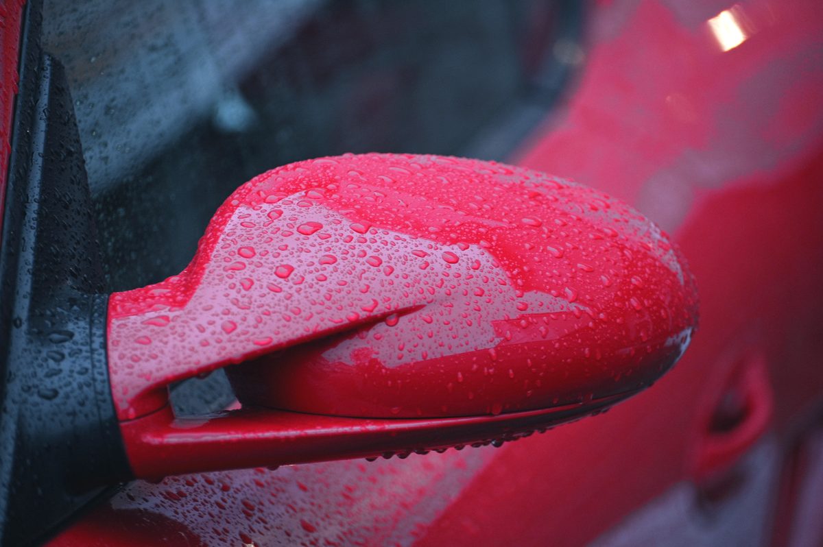 A red door mirror covered in raindrops.