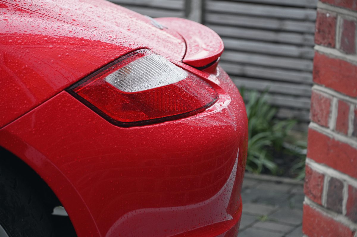 The rear lamp and wing of a red Cayman by a brick wall.