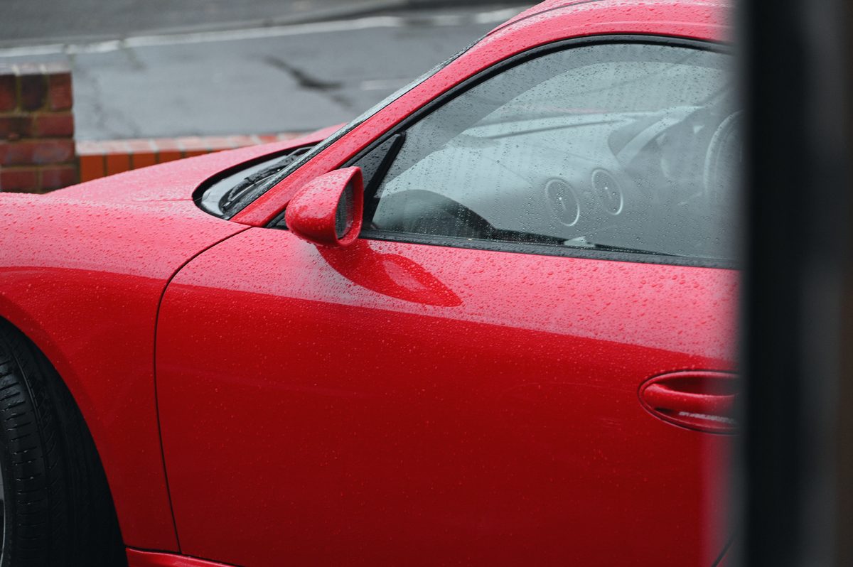The door and window of a red Cayman, seen past a gatepost.