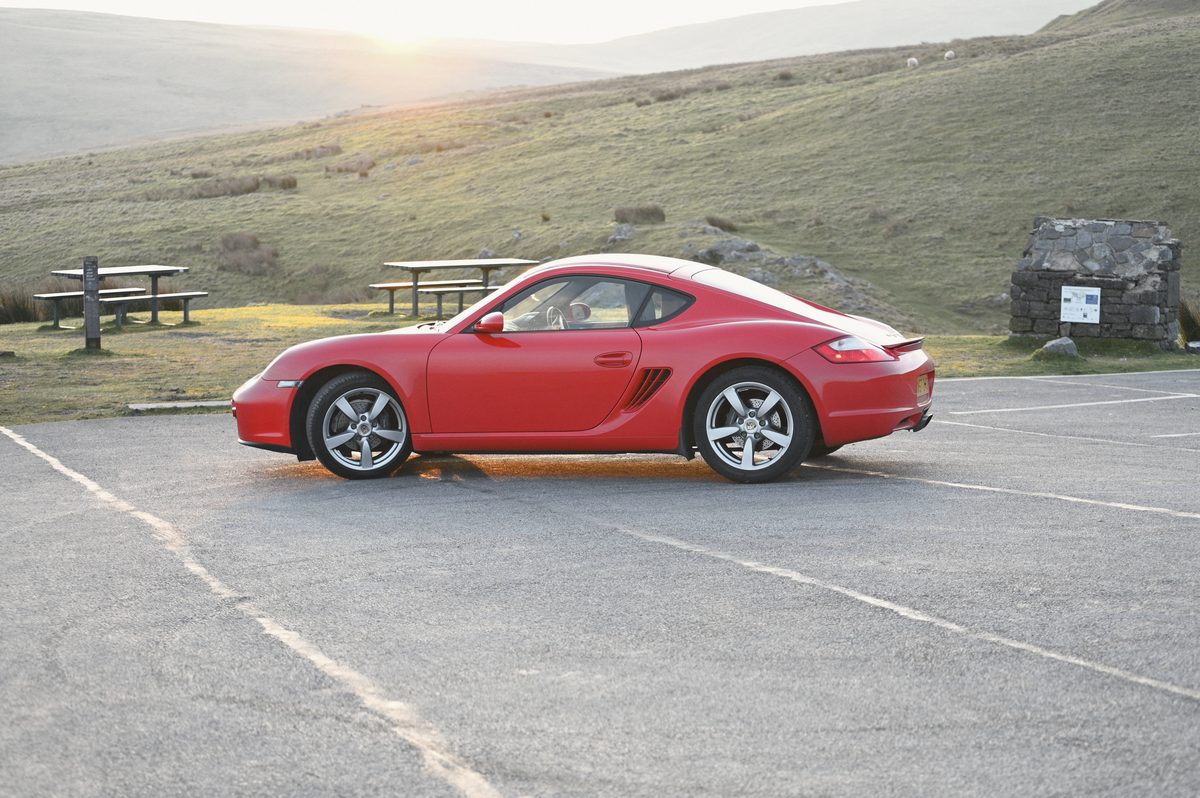 A red Cayman side on, the sun coming up over the hill behind.
