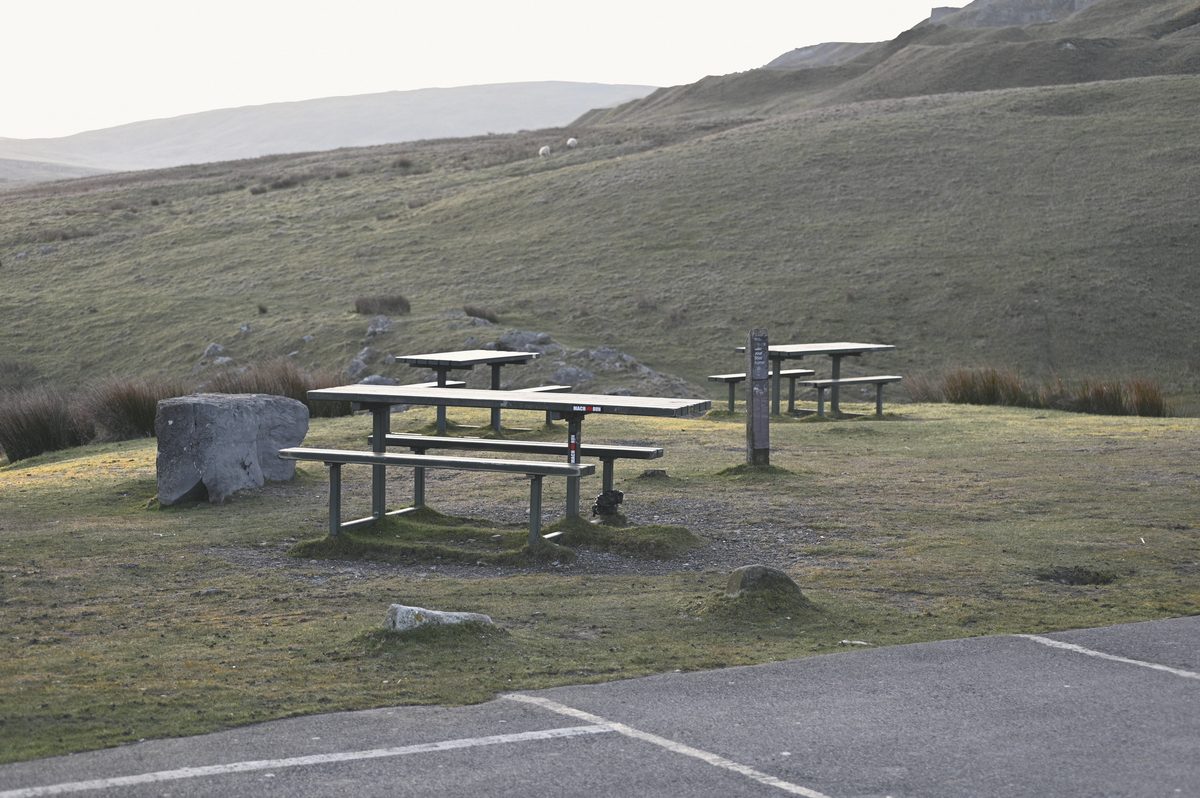Empty picnic benches on the grass by the car park.