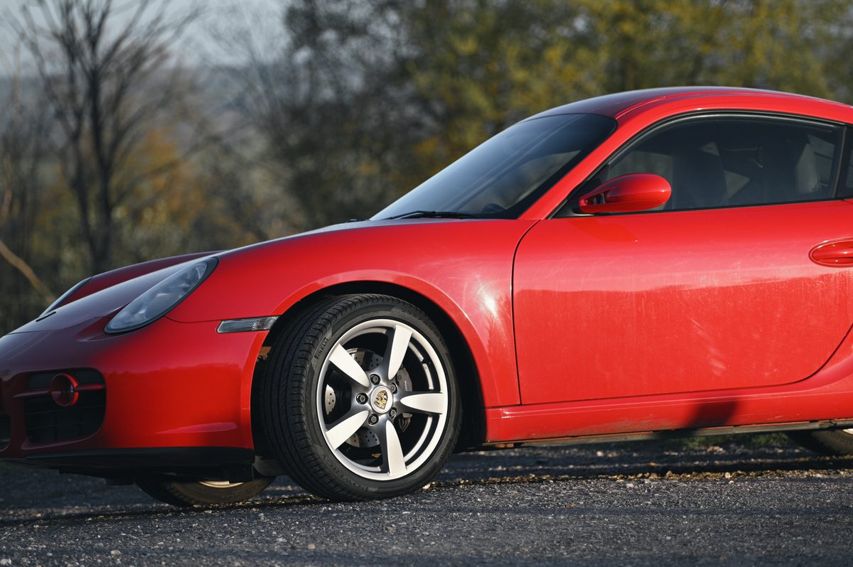 The front wheel and wing of a red Cayman, low and close, in morning sun.