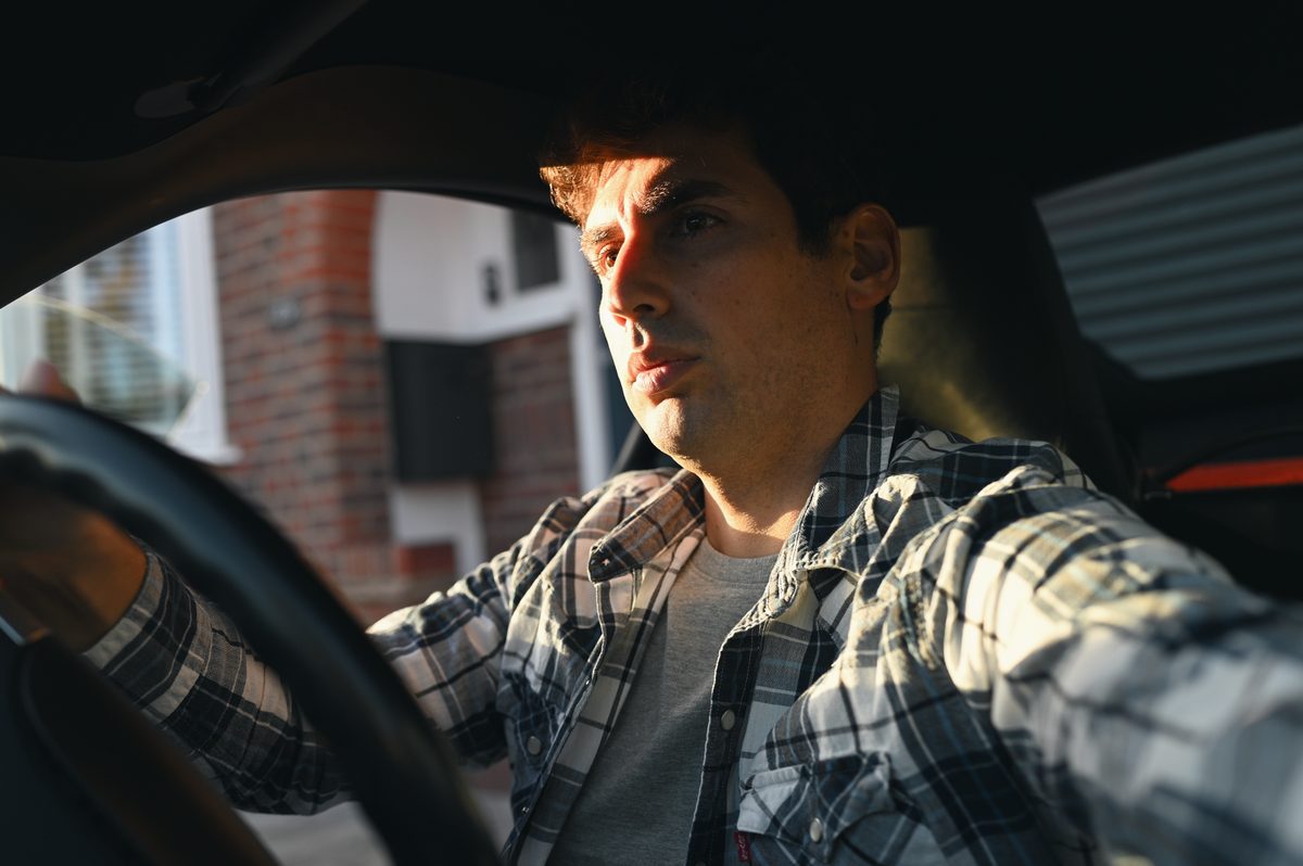 David at the wheel of his Cayman, a brick house through the window.