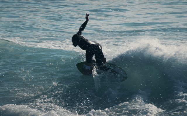 A skimboarder turns on the lip of a wave, one arm thrown up.