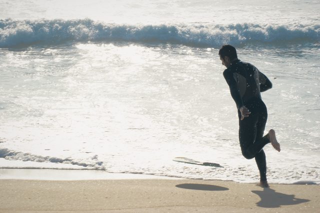 Backlit, a man sprints along the wet sand toward the water.