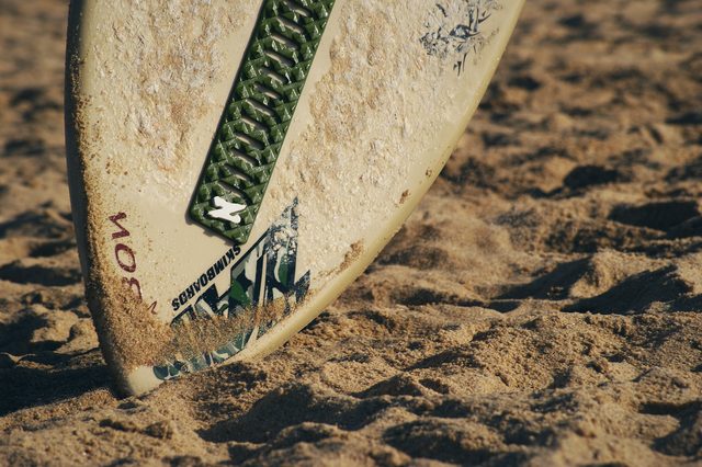 Close up, the worn grip and stickers on a board standing in the sand.