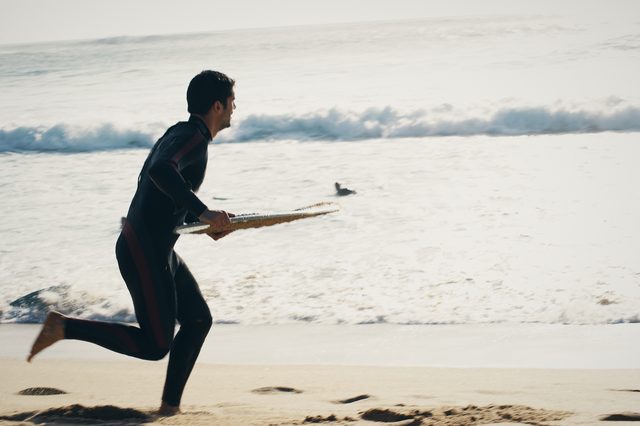 A man runs along the shore, board held out in front of him.