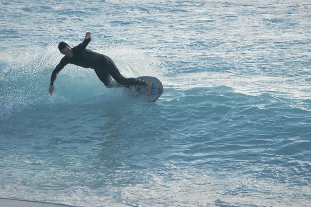 A skimboarder leans into a turn on a blue wave.