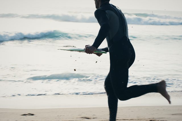 Mid-stride, a man about to drop his board on the wet sand.