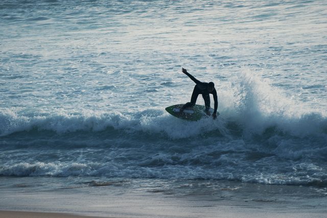 A rider on a green board turns at the top of a breaking wave.