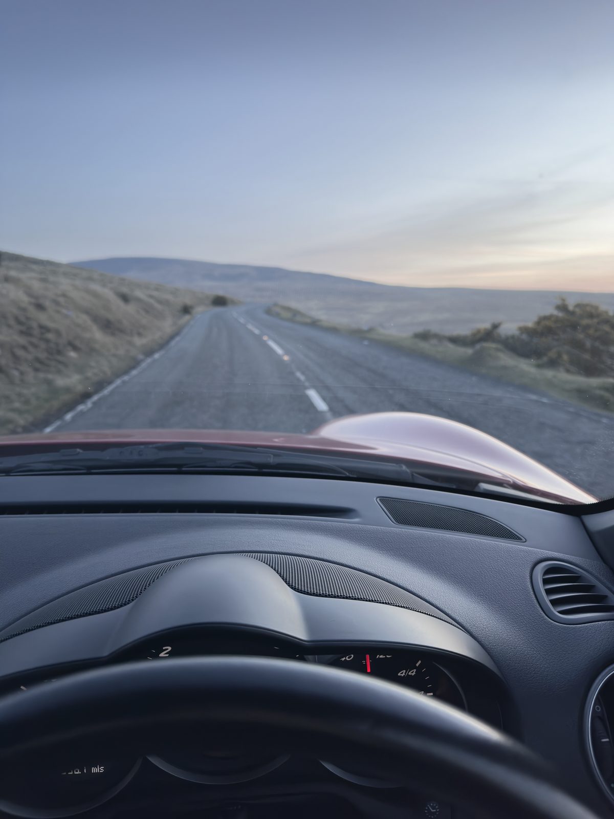 The empty road curving away across the moor, seen over the dashboard.