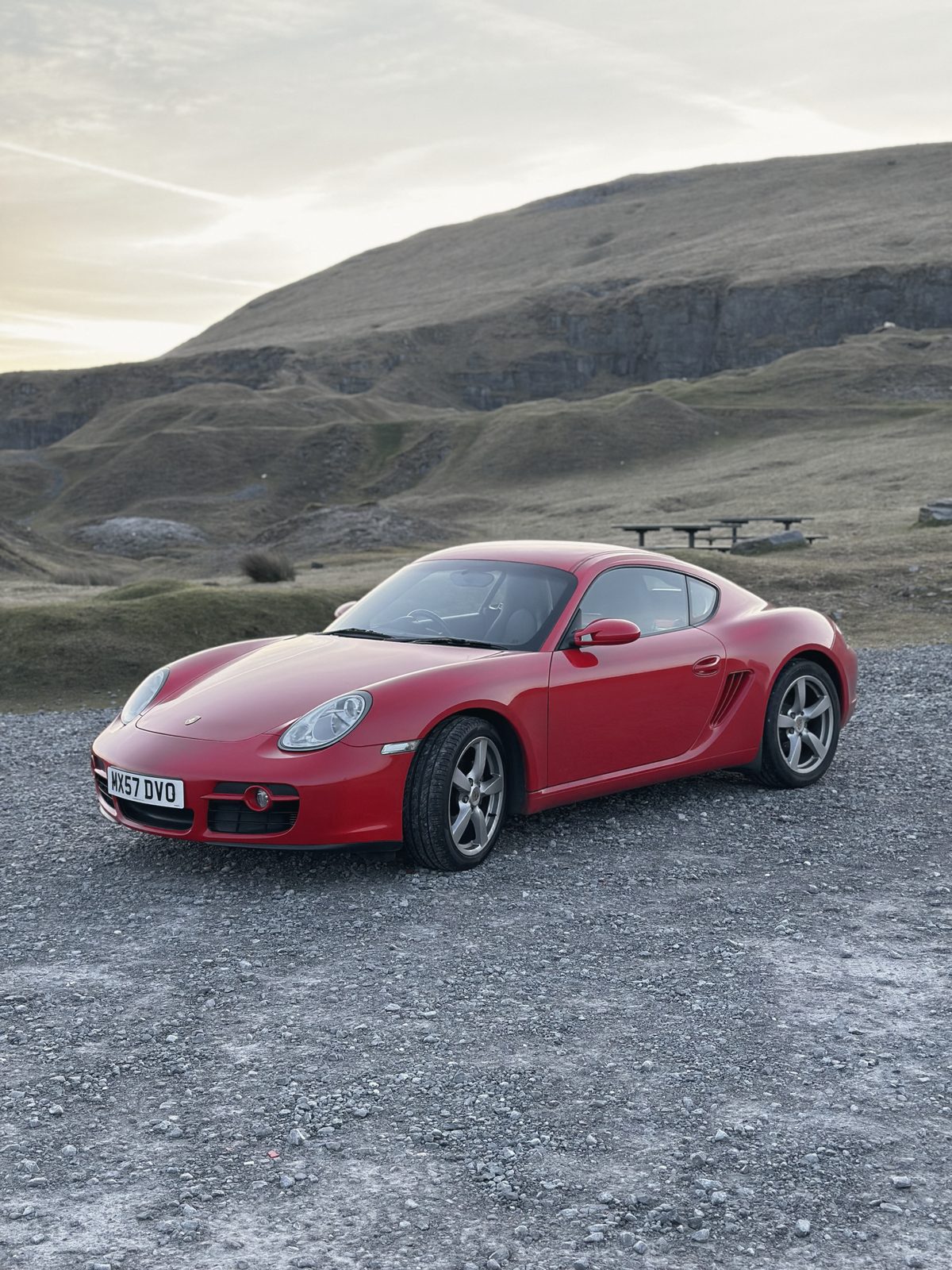 The red Cayman on the gravel, the quarried hillside behind.