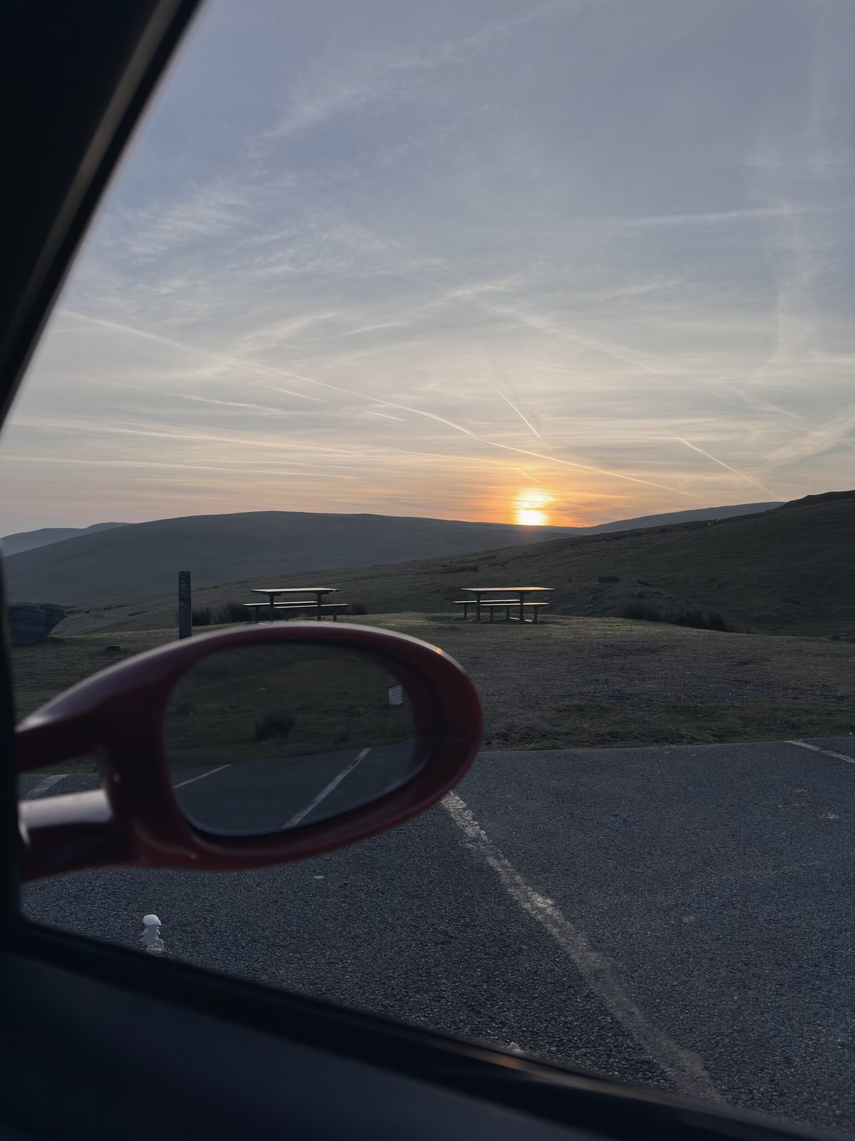 The sun clearing the hill, seen past the red door mirror, picnic benches below.