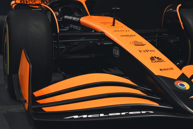 The papaya and black front wing of a current racing car, its stripes catching the light in a dark hall.