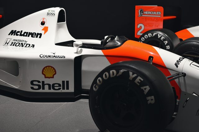 A white and red McLaren Honda racing car with Shell and Goodyear markings, close to the camera in a dark hall.