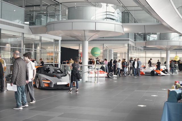 A bright glass atrium full of visitors walking between cars and displays.