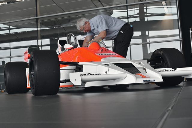 A man in a blue shirt leans over the cockpit of a white and red racing car from the 1970s.