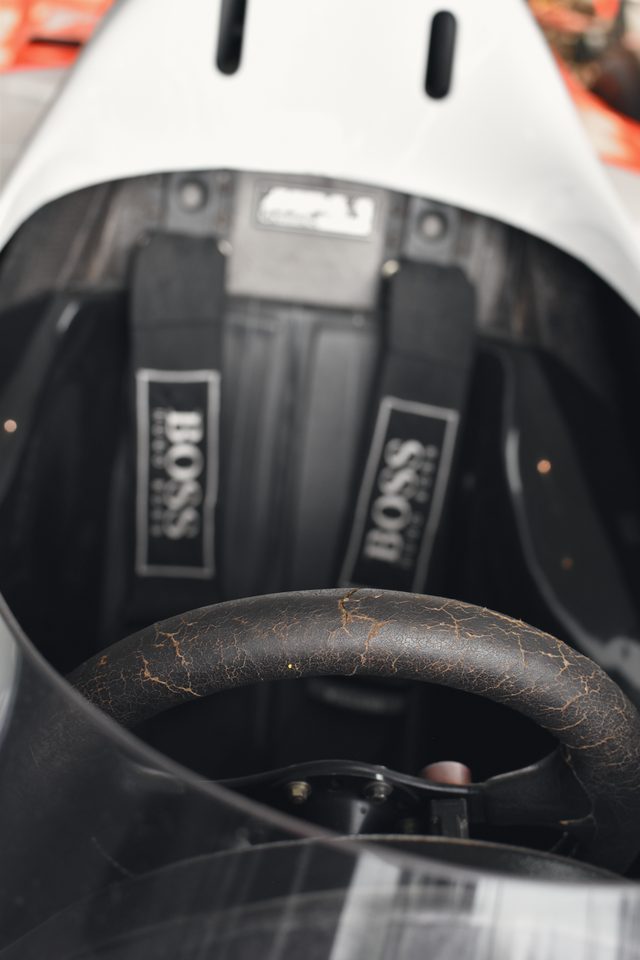 The worn leather steering wheel and the black harness straps in an old racing cockpit.