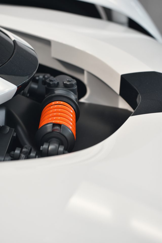 A bright papaya spring tucked inside the white bodywork of a car.