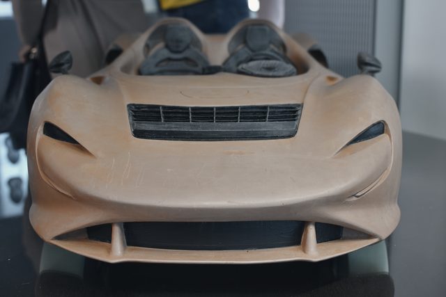 A full-size clay model of a sports car, seen head-on.