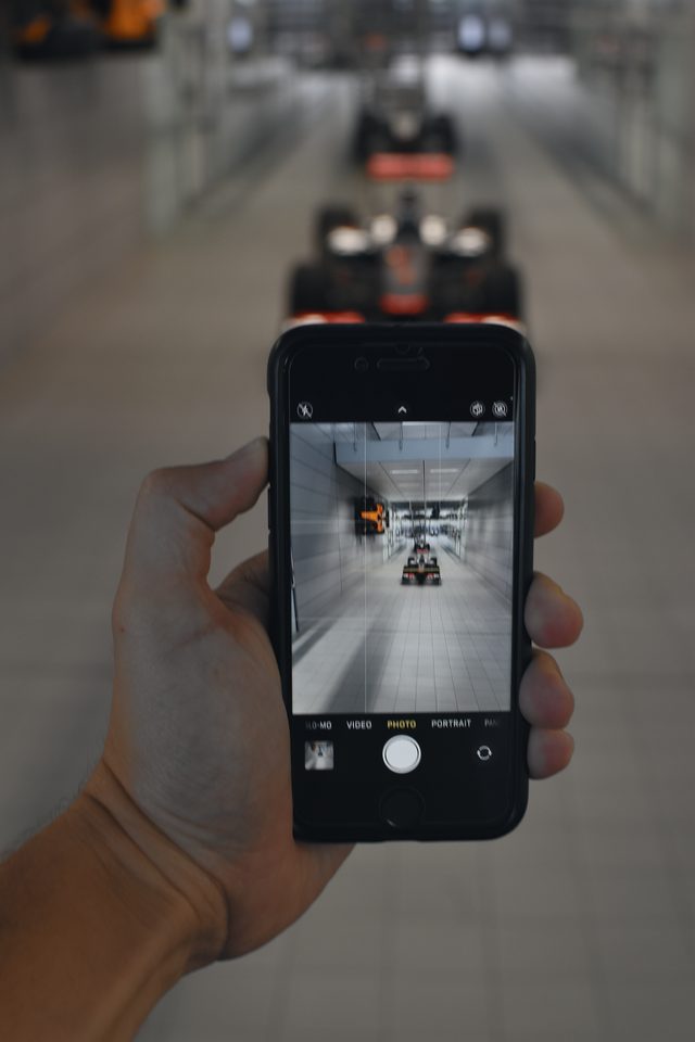 A hand holds up a phone, photographing the corridor of racing cars.