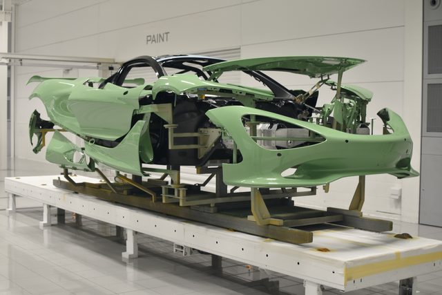 A car body shell, without doors or engine, sits on a frame on the factory floor under a sign that reads Paint.