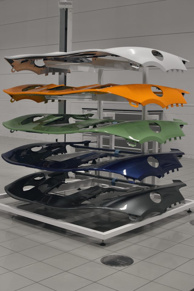 A rack of painted body panels in white, papaya, green, blue and black on the factory floor.