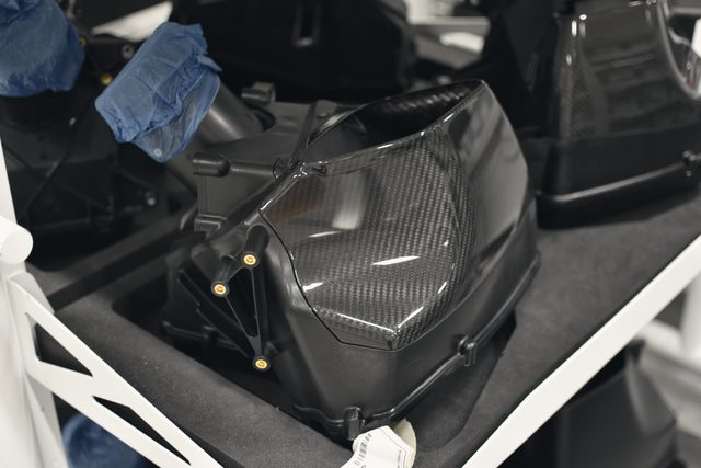 Hands in blue gloves work on a carbon fibre tub on the factory floor.