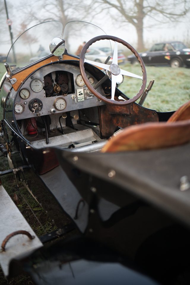 The cockpit of a vintage racing car: a wooden steering wheel, brass dials and worn leather.