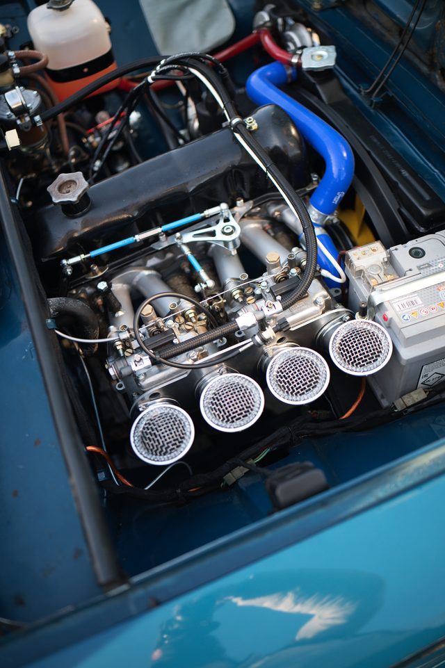 Four polished air trumpets on the engine of a blue car, its bonnet open.