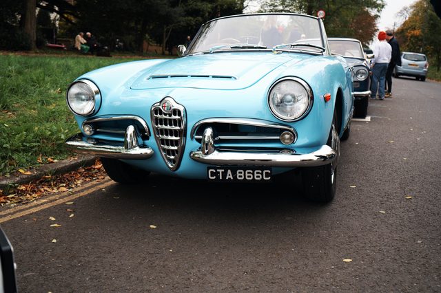 A pale blue Alfa Romeo convertible parked on a quiet road in autumn.