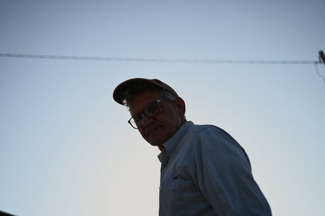 A man in a cap and glasses, seen from below against the sky.