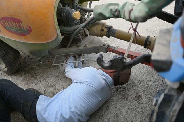 A man lies on his back under the tractor, working on the hitch.