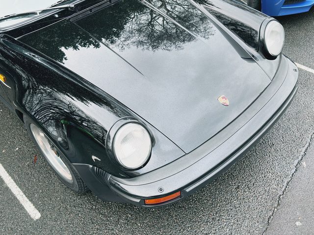 The bonnet and headlight of a black classic Porsche, bare trees reflected in the paint.